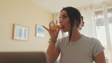 Fototapeta premium Young woman working on laptop at home and drinking juice from glass