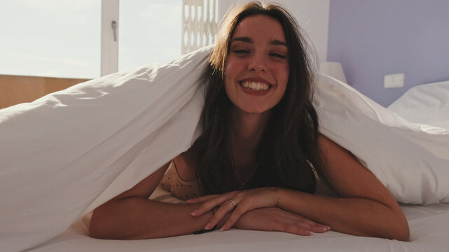 Close-up, Happy Girl Posing In Bed. Laughing Girl Peeps Out From Under The Blankets