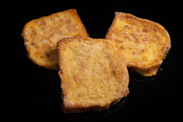 (Torrijas) Fried bread soaked in milk flavored with vanilla, cinnamon, lemon and egg on a black background. Typical Easter sweet. Concept of traditional and festive cuisine.