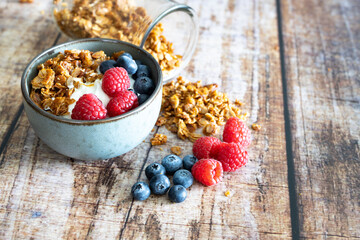 granola with raspberries and blueberries with yogurt on a wooden background