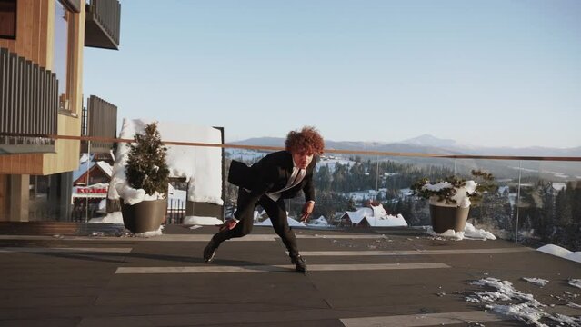 A stylish young male dancer in a classic black suit dances against the backdrop of snowy mountains on the terrace.The concept of modern dance