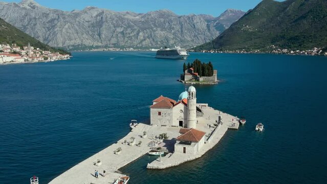 Aerial view famous historical island with church in Kotor bay near Perast city, large cruise ship goes on a background. Mountain landscape around