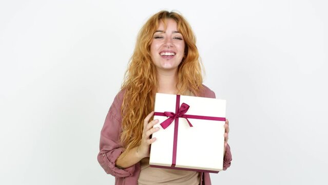 Young redhead woman happy and holding a gift over isolated background