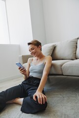 Freelance woman with laptop and phone works from home sitting on the floor in her home clothes with a short haircut, free copy space