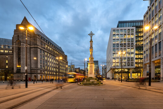 Metro tram passing beside St Peter cross in St Peter Square at  Manchester town hall, England