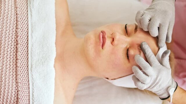 Beautician cosmetologist makes a procedure on the face with microcurrent therapy gloves. Hardware cosmetology in clinic salon for client.