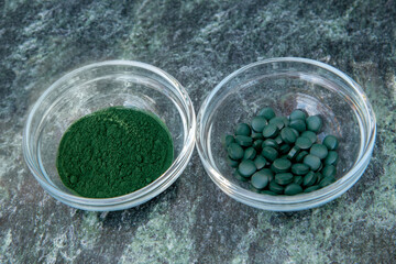 Obraz na płótnie Canvas spirulina powder and tablets in glass bowls on a green marble background