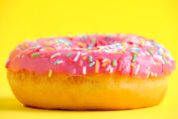 Donut with pink icing and multicolored sugar sprinkles.On yellow background,closeup.