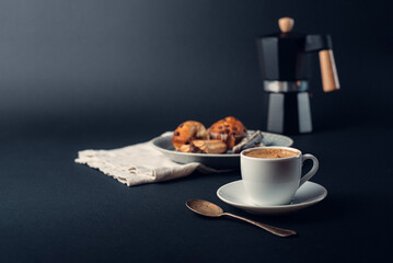 Taza de café con cuchara de cobre, con plato con galletas y muffins de chocolate, cafetera italiana, sobre fondo azul oscuro
