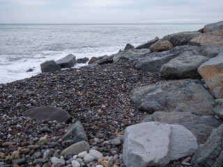 Fototapeta na wymiar resort in winter. The rocky shore is washed by the waves in cloudy weather. Black Sea coast. The coast of Batumi. Nature in shades of grey. boring landscape