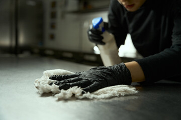 Woman in protective gloves washes cutting table in restaurant kitchen