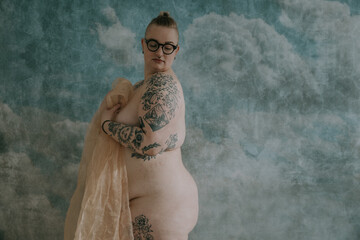 plus size non-binary person with tattoos standing sideways holding fabric