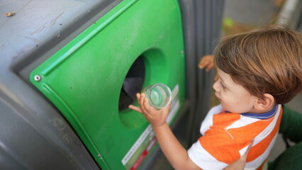 Child recycling glass bottle into recycle bin dispenser. Kid putting bottle inside recycle object