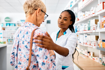 Obraz na płótnie Canvas Caring African American pharmacist consoling sad senior woman in drugstore.