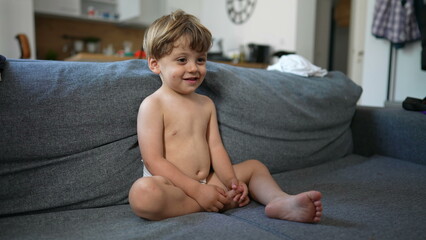 Baby toddler sitting on couch wearing diapers watching Television. One little boy