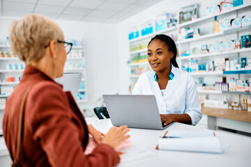 Young black pharmacist talks to her senior customer in drugstore.