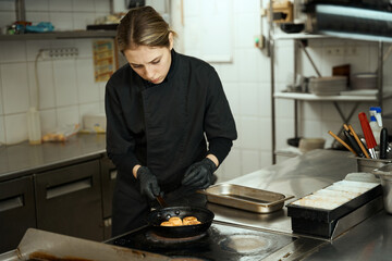 Female chef fries cheesecakes in a cast iron pan on a large stove