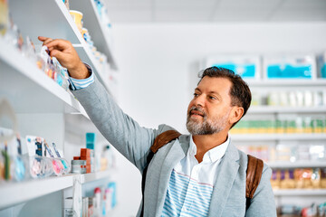 Middle aged man looking for vitamins on shelf while shopping in pharmacy.
