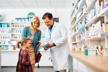 Happy mother and daughter using touchpad with their pharmacist in pharmacy.
