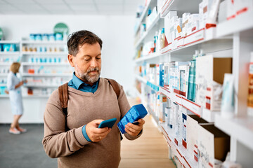 Middle aged man using cell phone while buying in pharmacy.