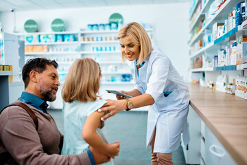 Naklejka na ściany i meble Happy pharmacist talks to little girl and her father in pharmacy.