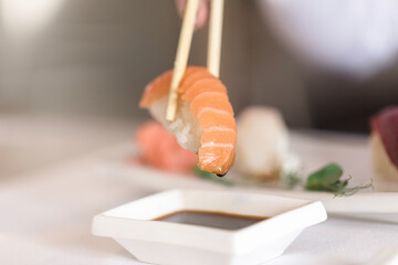 A hand holding a piece of juicy salmon nigiri, garnished with a dollop of wasabi. Sushi platter...