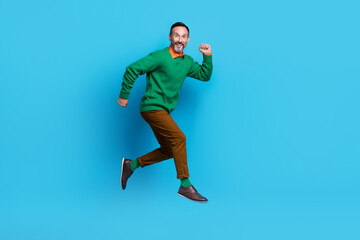 Obraz premium Full length photo of mature nice mister energetic running jumping rush dressed stylish green outfit isolated on blue color background