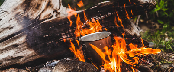 Kettle hanging over fire. Cooking food at fire in wild. Beautiful big log burns in bonfire...
