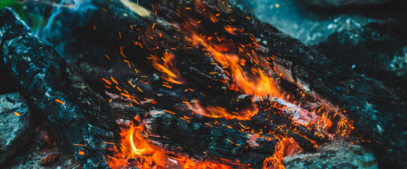 Vivid smoldered firewoods burned in fire closeup. Atmospheric background with orange flame of...