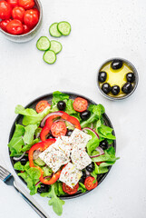 Vegetable greek salad with feta cheese, olives, tomatoes, paprika, cucumber and red onion, healthy mediterranean food, low calories eating. White stone background, top view