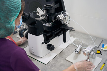 Doctor under microscope with micromanipulator carries out fertilization of egg