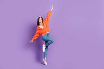 Fototapeta na wymiar Full length photo of carefree sweet woman dressed orange jumping high arms sides empty space isolated purple color background