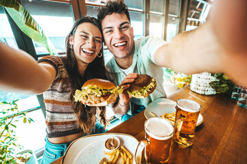 Happy couple taking selfie with smart mobile phone at burger pub restaurant - Young people having...
