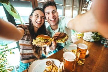 Fotobehang Happy couple taking selfie with smart mobile phone at burger pub restaurant - Young people having lunch break at cafe bar venue - Life style concept with guy and girl hanging out on weekend day © Davide Angelini