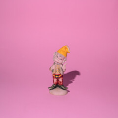 Garden gnome, a small figurine of  elf dwarf, a wise man, with a yellow cat, and red pants on a pink background.