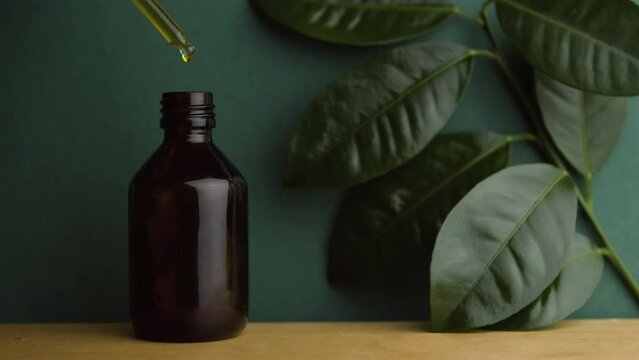 Natural oil. Alternative medicine. Handmade cosmetics. A pipette with oil. Dark glass bottle on a wooden table. Background from natural leaves. A drop of oil.  Face and body skin care. 