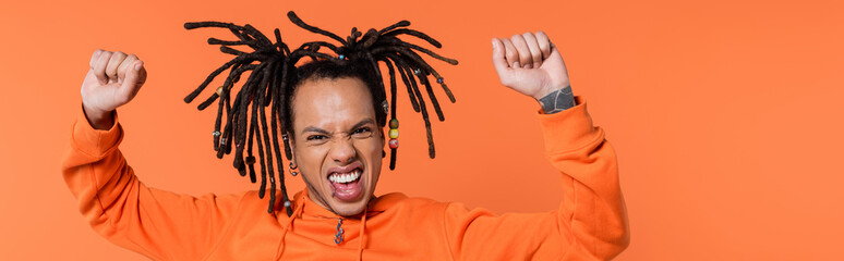excited multiracial man with tattoo celebrating isolated on coral, banner