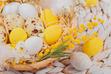 Easter candy chocolate eggs and almond sweets lying in a bird's nest decorated with flowers and feathers on white background. Happy Easter concept.
