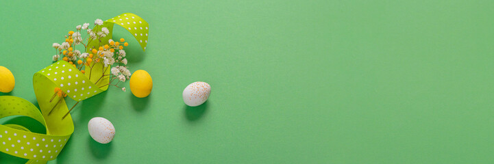 Minimalistic easter floral background made of chocolate candy eggs, flowers and ribbon on green background. Panoramic long banner