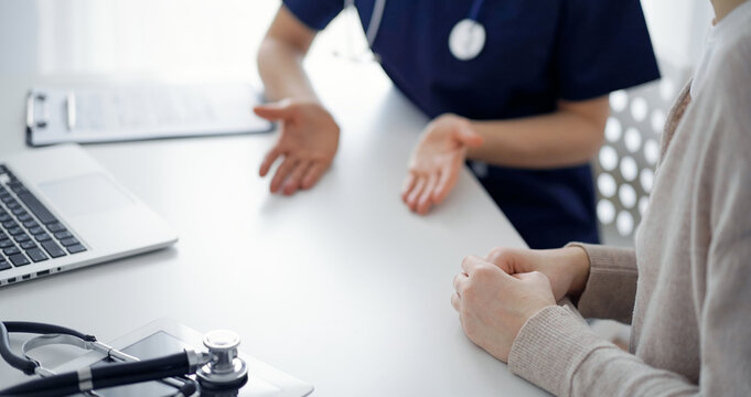 Doctor and patient sitting at the table in clinic while discussing something. The focus is on female patient's hands, close up. Medicine concept