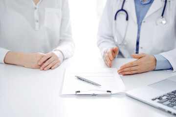 Doctor and patient discussing current health questions while sitting near of each other at the table in clinic, just hands closeup. Medicine concept