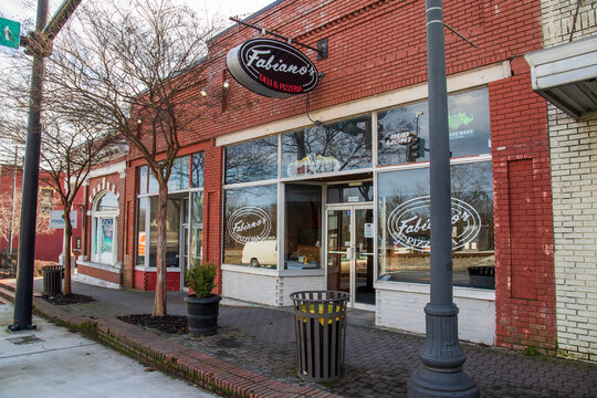 Fabiano’s Deli and Pizzeria in a red brick building along Veterans Memorial Hwy with bare winter trees and metal trash cans along the sidewalk on a cloudy day in Douglasville Georgia USA
