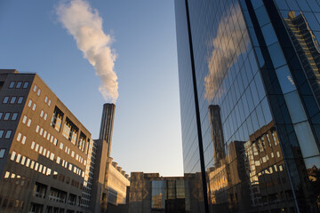 cheminée et fumée d'un chauffage urbain se reflétant dans les vitres d'un immeuble - obrazy, fototapety, plakaty