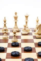playing by different rules on the same board - black checkers and white chess figures on wooden chessboard, gameboard with chess and checkers playing closeup (focus on front checkers disc)