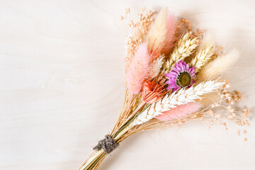 top view of tied bouquet of dried flowers and spikelets on light brown wooden background with...
