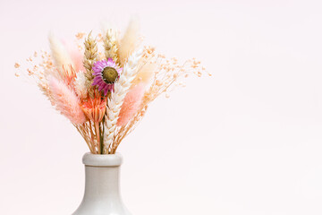 bouquet of dried flowers and spikelets in neck of ceramic bottle on light pink background with copyspace