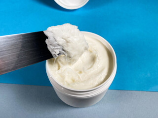 white jar with cream and spatula close up on blue colour papers background