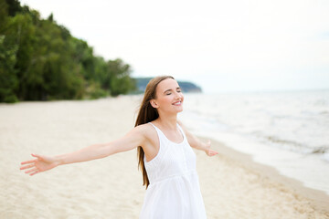 Fototapeta na wymiar Happy smiling woman in free happiness bliss on ocean beach standing with open hands. Portrait of a multicultural female model in white summer dress enjoying nature 