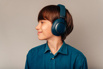 Side view portrait of a smiling teen boy wearing blue shirt and headphones over grey background.