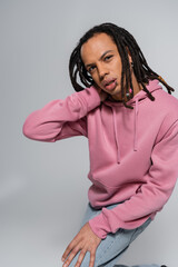 Fototapeta premium pierced multiracial man with dreadlocks looking at camera and posing on grey